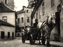 Uliczka przedwojennego Wilna. Na pierwszym planie widoczny powóz konny z uśmiechniętą pasażerką.